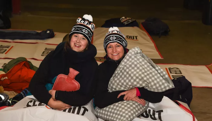 Two people holding hot water bottle and pillow in Sleep Out woolly hats