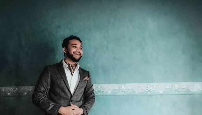 Young person smiling wearing a grey suit against a teal coloured wall
