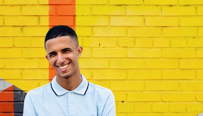 Young person smiling against a yellow brick wall