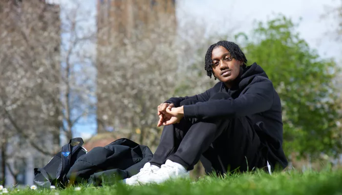 Young person outside sitting on the grass with their rucksack