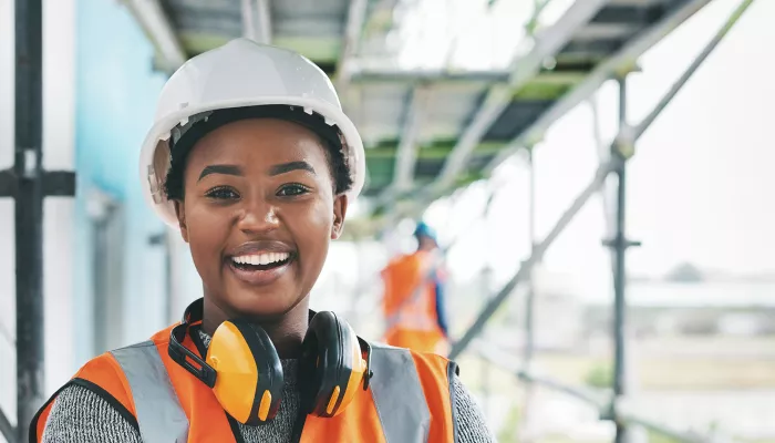 Young person wearing a hard hat on a construction site smiling and looking directly at the camera