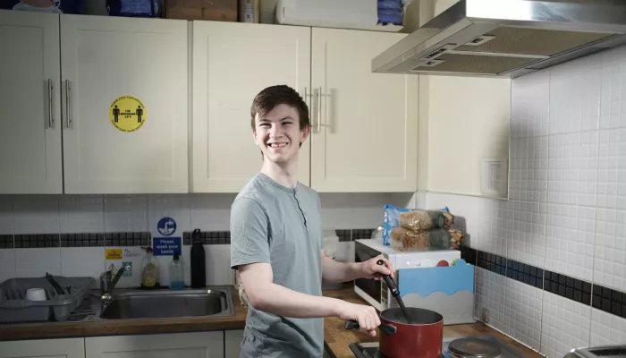 Young person wearing a t-shirt smiling and cooking