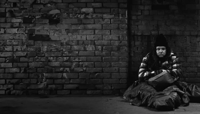 black and white image of Mia who is sat outside on the floor, with a sleeping bag, looking cold and homeless