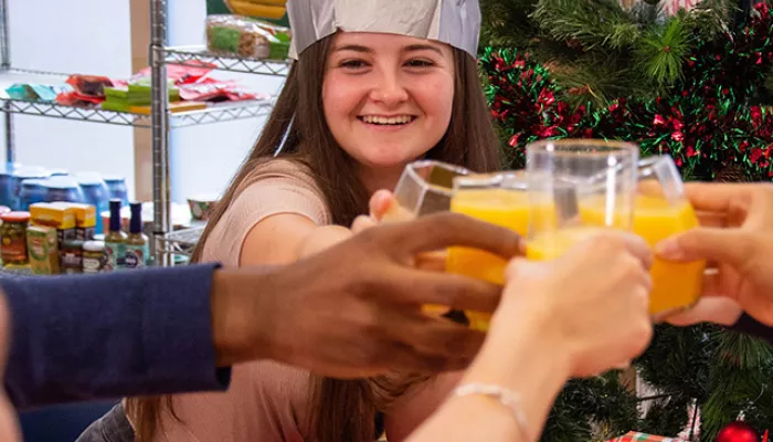 Young people sit around a dinner table wearing Christmas paper crowns, raising their glasses of orange juice for a toast