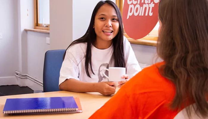 A Centrepoint support officer and a young person sit at a table, drinking a hot drink and chatting