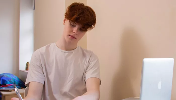 A young person is concentrating hard as they study, writing notes and reading from a textbook