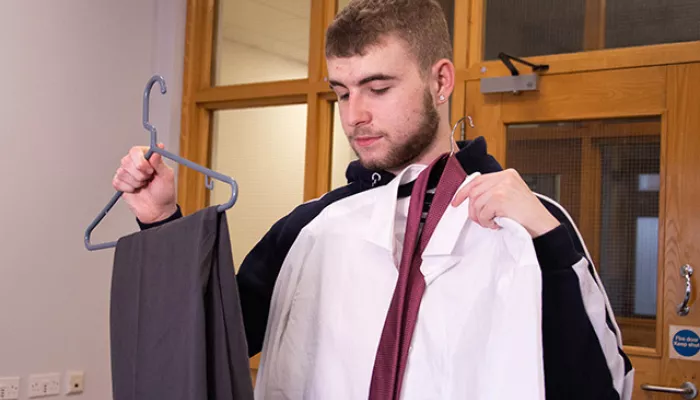 A young person holds up new, smart clothes for work - a pair of grey trousers and a white shirt