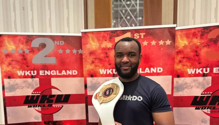 Young person holding a martial arts trophy belt over shouder