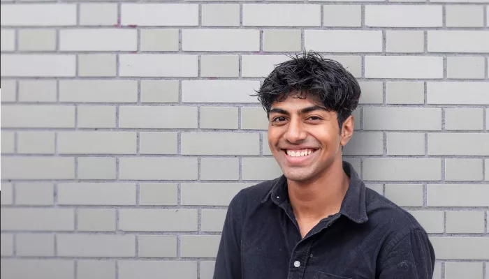 smiling young person standing against a grey brick wall