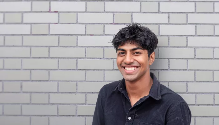 smiling young person standing against a grey brick wall