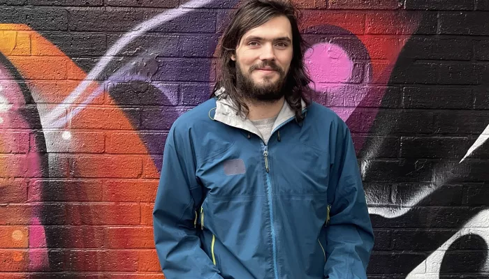 A young man leans against a wall, looking happy.