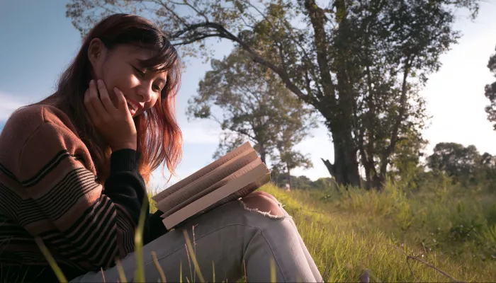 young person sitting in the park with a book