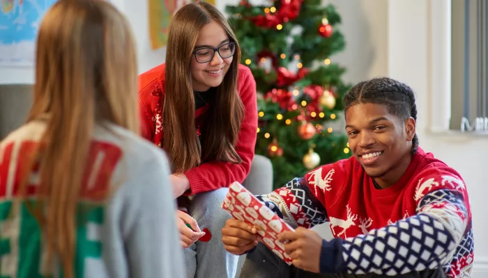 A group of young people sit around a Christmas tree and exchange gifts