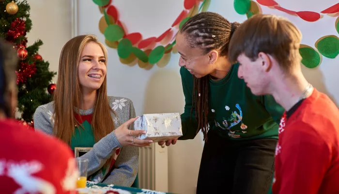 A group of young people receive gifts for Christmas, smiling next to the tree