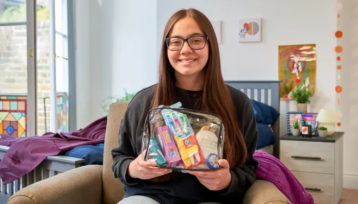 A young person sits in a Centrepoint service, smiling at the camera and holding a collection of toiletries