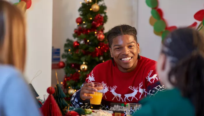 A young person wearing a festive red jumper sits at the dinner table enjoying a Christmas dinner