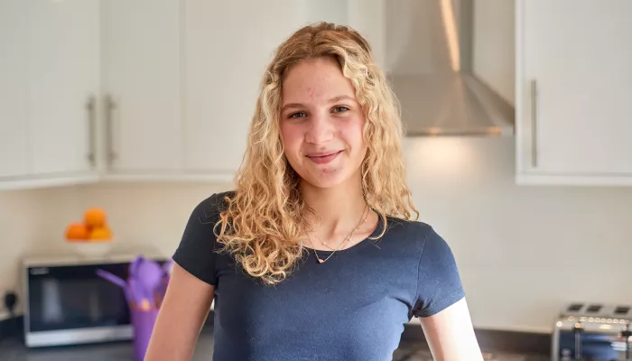 A young person smiles while standing in her kitchen at home