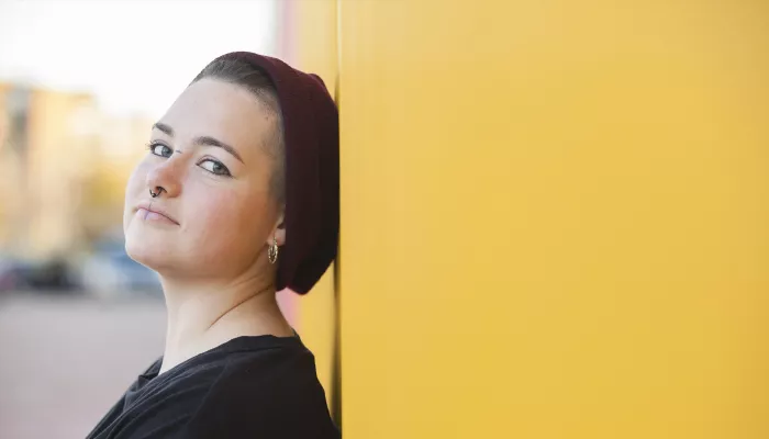 Young person wearing beanie hat standing against a yellow wall