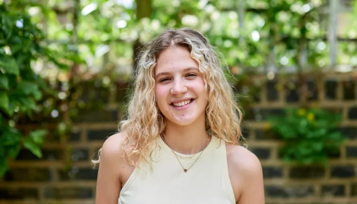 A young person stands outside and smiles at the camera