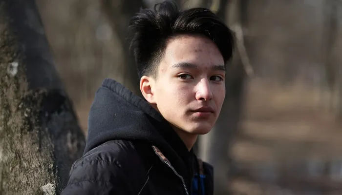 Young man in woody park looking over his shoulder to the viewer.