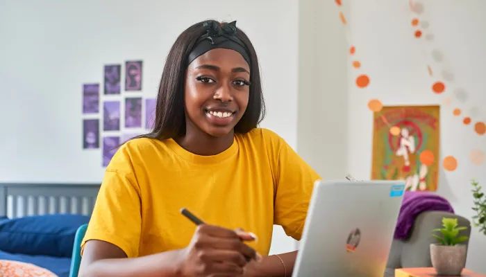 Young person smiling to camera whilst sitting at a desk with a laptop