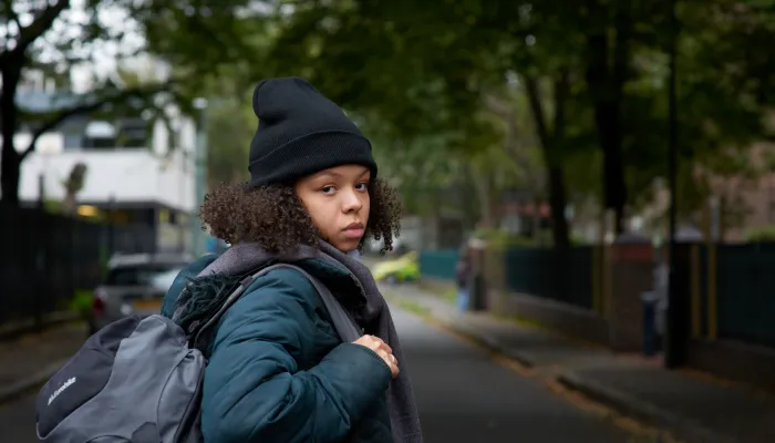 A young homeless person carries a backpack outside on a chilly day