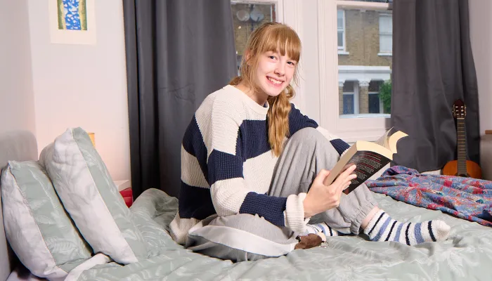 A young person sits on a bed reading in supported accommodation