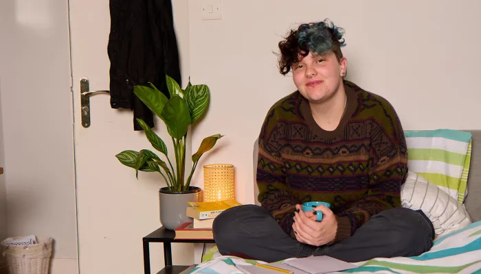 A young person sits on a bed in their supported accommodation