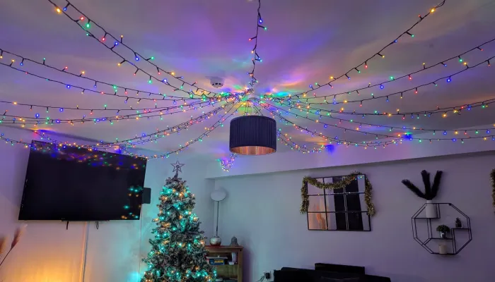 Colourful Christmas lights adorn the ceiling of a living room, with a Christmas tree in the background