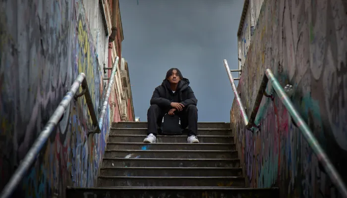 A young person sits at the top of the stairs of an underpass