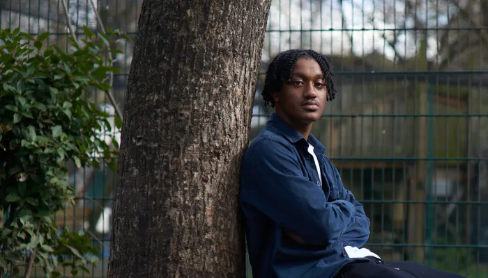 A young person sits in a park, leaning against a tree