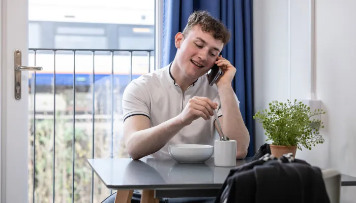 Young person on phone sitting stirring a cup of tea