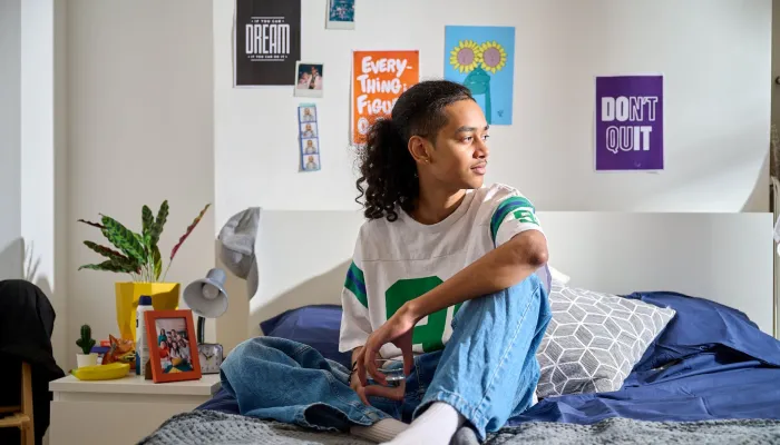 A young person sits on a comfortable bed in their supported housing