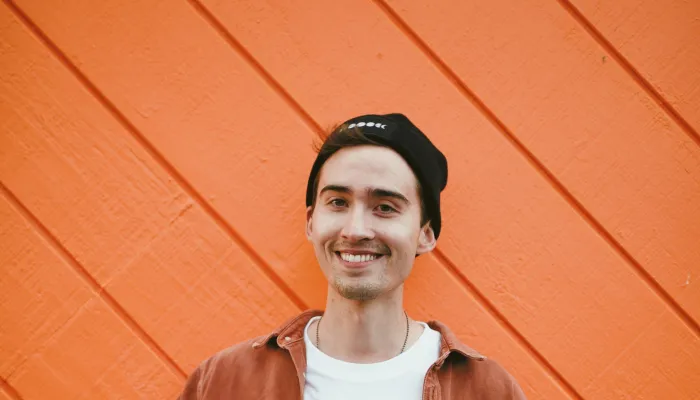 Young man smiling in front of an orange wall