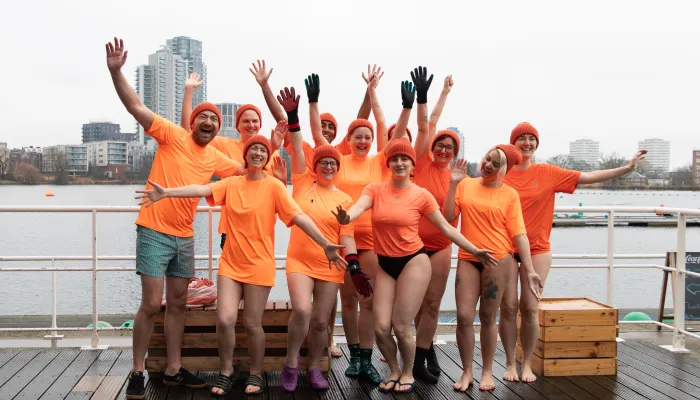 Group of people wearing orange T shirts, raising their hands in the air and cheering.