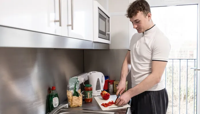 A young person prepares food in a kitchen in their new home
