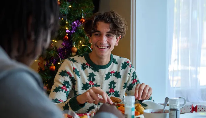Young people wearing festive jumpers smile while eating their Christmas dinner at the table