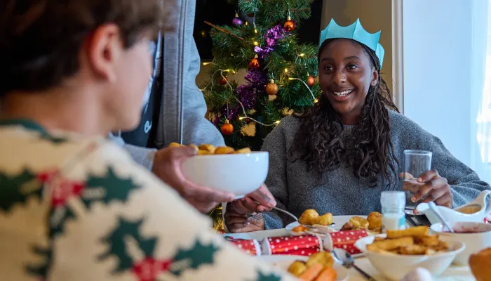 Young people enjoy a christmas dinner at the table, smiling and wearing paper crowns from crackers