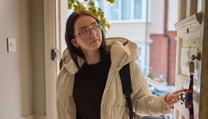 A young person opens the front door and walks into their new flat for the first time