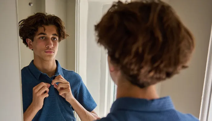 A young person gets dressed in new smart clothes in front of a mirror