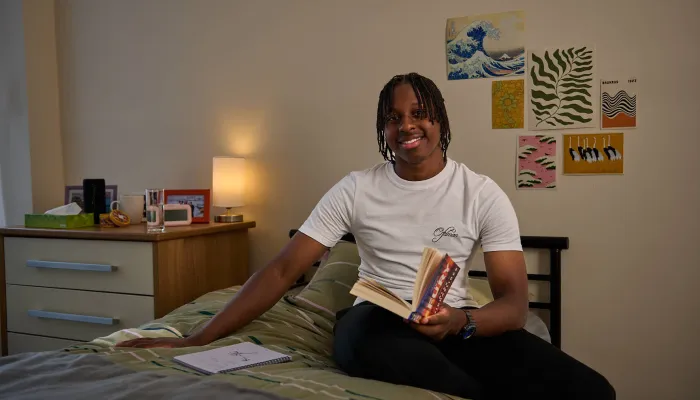 A young person smiles sitting on their bed in their cosy room at a Centrepoint service.