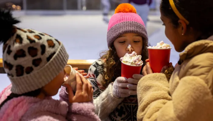 A group of children in warm hats and coats stand together and drink a luxurious takeaway hot chocolate