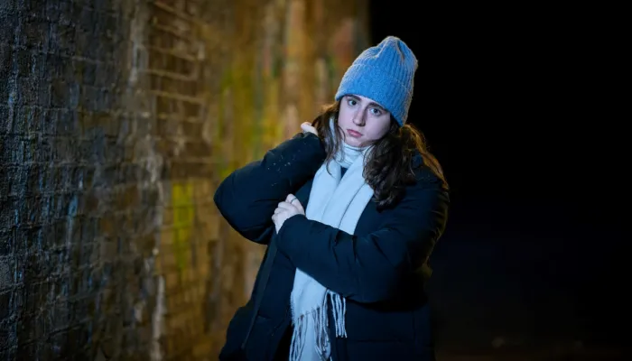A girl wrapped up in a warm coat and scarf, standing outside and looking directly at the camera.