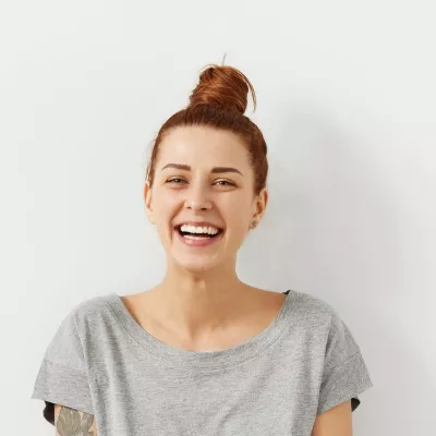 Young person stands against white wall whilst smiling at the camera