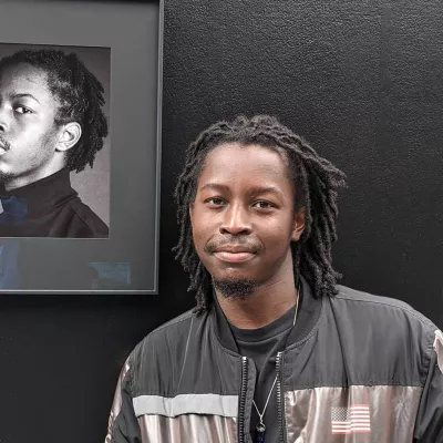 Young, Black young person with long braids stands in front of a portrait of themselves