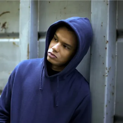 Young mixed race person in blue hoodie leaning against concrete wall