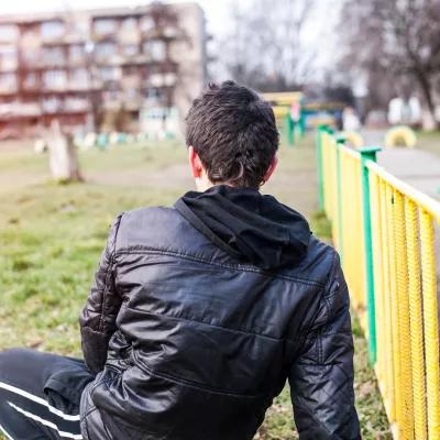 person sitting on grass with back to the camera looking towards a block of flats