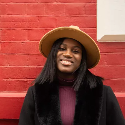 Young person wearing a wide-brimmed hat in front of red brick wall