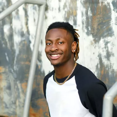 young black person with braids in a white and navy t-shirt in front of a wall