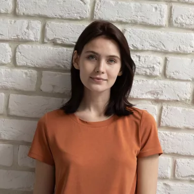 Young person with long dark hair in an orange t-shirt against a white brick wall